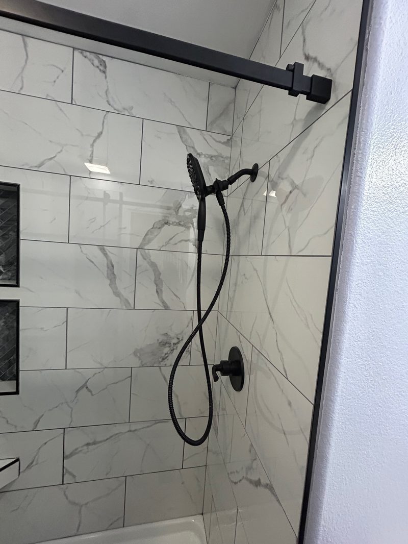 Black matte handheld shower fixture installed on marble-look tile wall