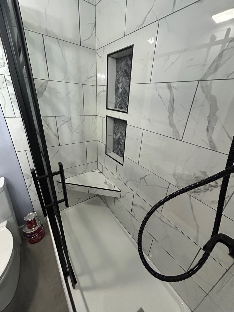 Marble-look tile shower with black-frame glass door and built-in niches in a Utah County bathroom remodel